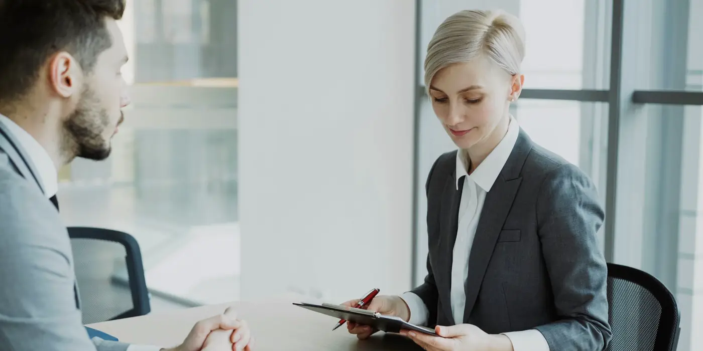 Professional with a tablet listening to a client across a desk in a bright, modern office
